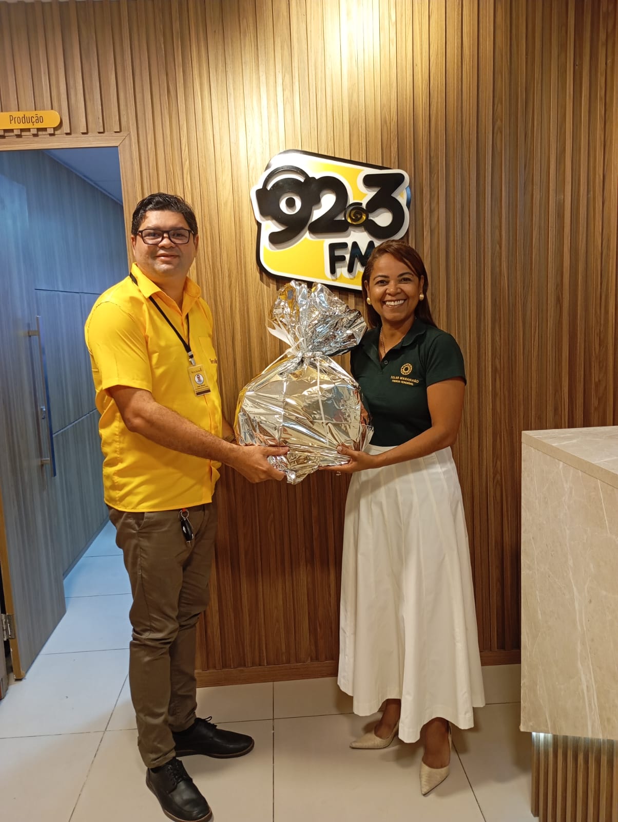 João Baima recebe o prêmio embrulhado das mãos de Ana Cristina, da Solar Maranhão, diante do logo da 92.3 FM